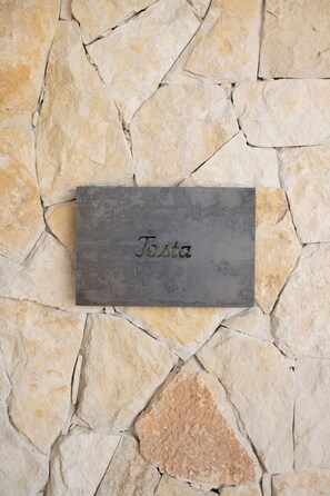 Un mur de pierre sur lequel est fixée une plaque portant l’inscription « Testa ».
