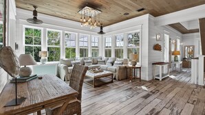 Una habitación amplia con techo de madera, ventanas grandes, una zona de estar acogedora con sofá y sillones, una mesa de madera y una mesa de comedor.