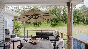 A covered outdoor patio with a table, chairs, a grill, and a large umbrella. - The Lake Escape - Sauna & Spa (Conjola Park)