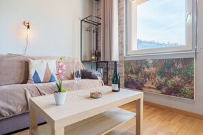 Ein Wohnzimmer mit einem beigefarbenen Sofa, einem Holztisch, zwei Weingläsern, einer Weinflasche und einer Orchidee im Topf.