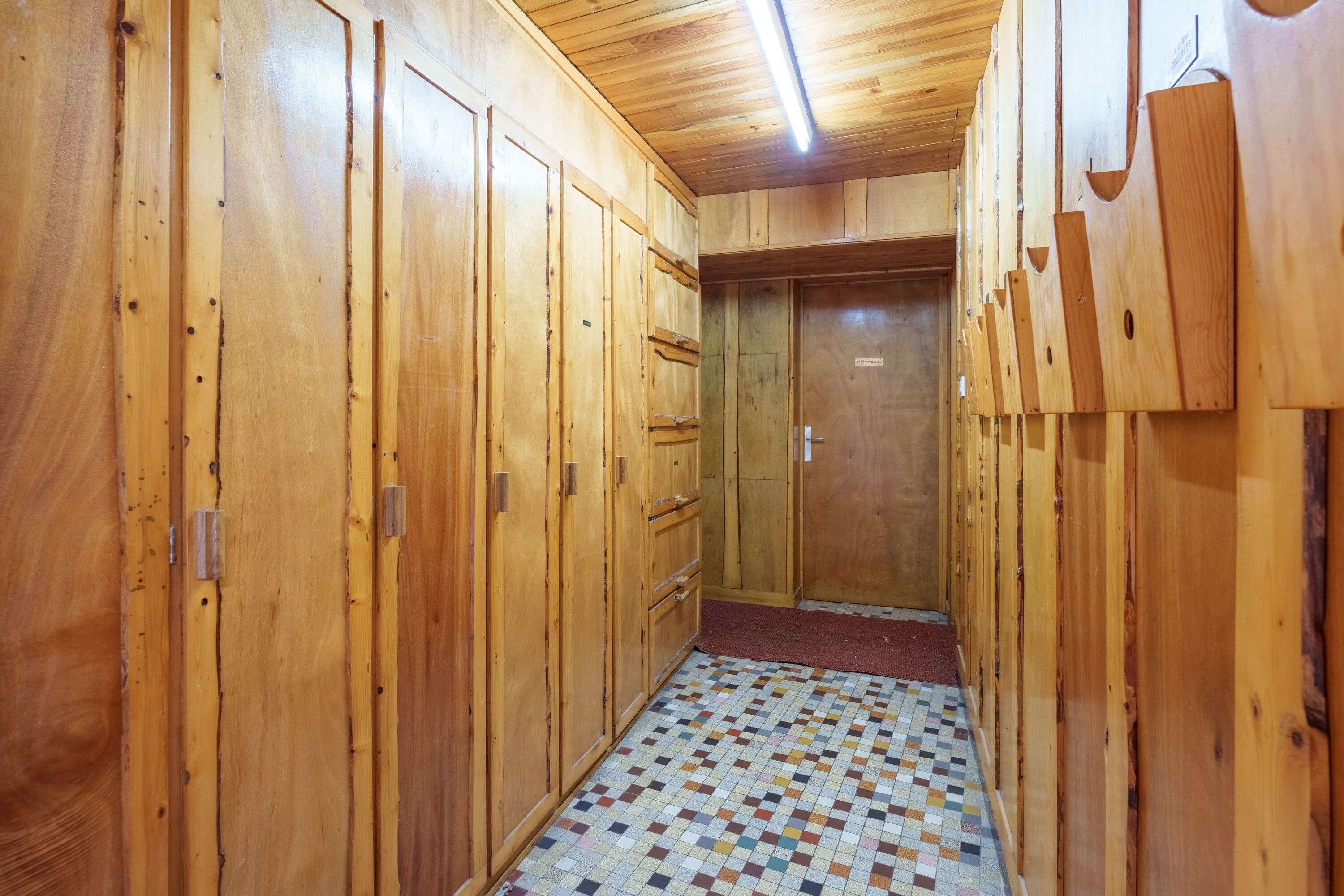A wooden hallway with a tiled floor and a door at the end.