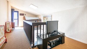A room with a bunk bed, a flat-screen TV on a stand, a carpeted floor, and a door leading outside.