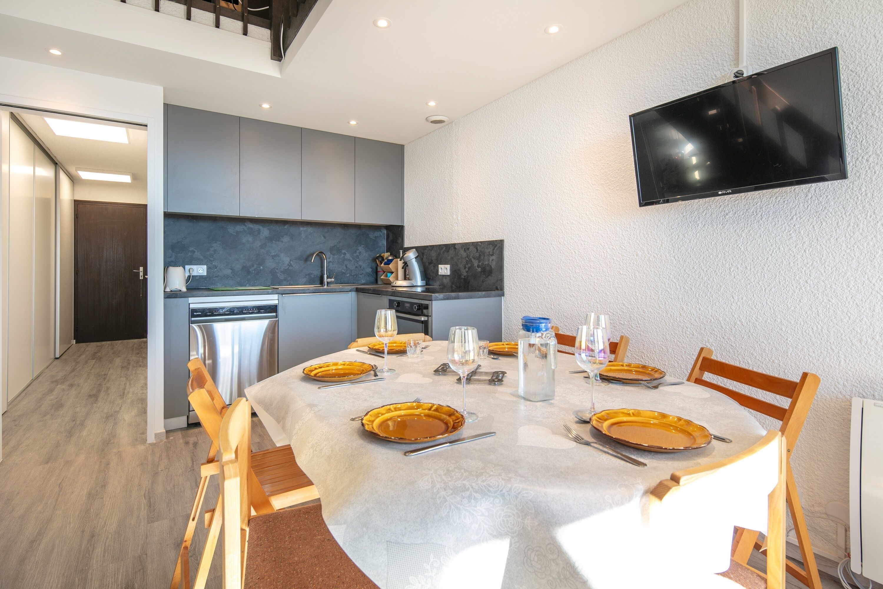 Eine moderne Küche mit grauen Schränken, einem Einbauofen und einem flachbildfernseher an der Wand.