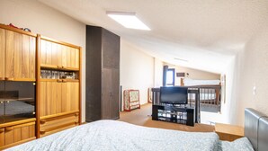 A bedroom with a bed, a TV, a wooden wardrobe, and a desk with a chair.