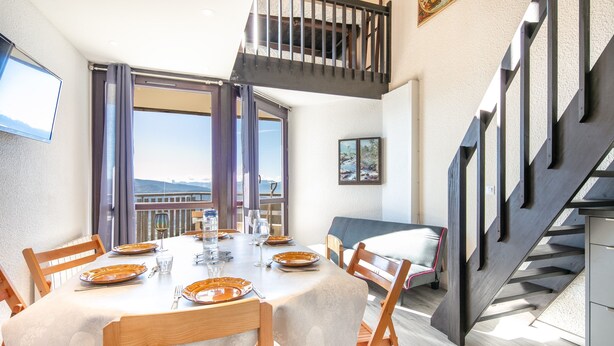 A dining area with a table set for four, a staircase, and a balcony with a view.