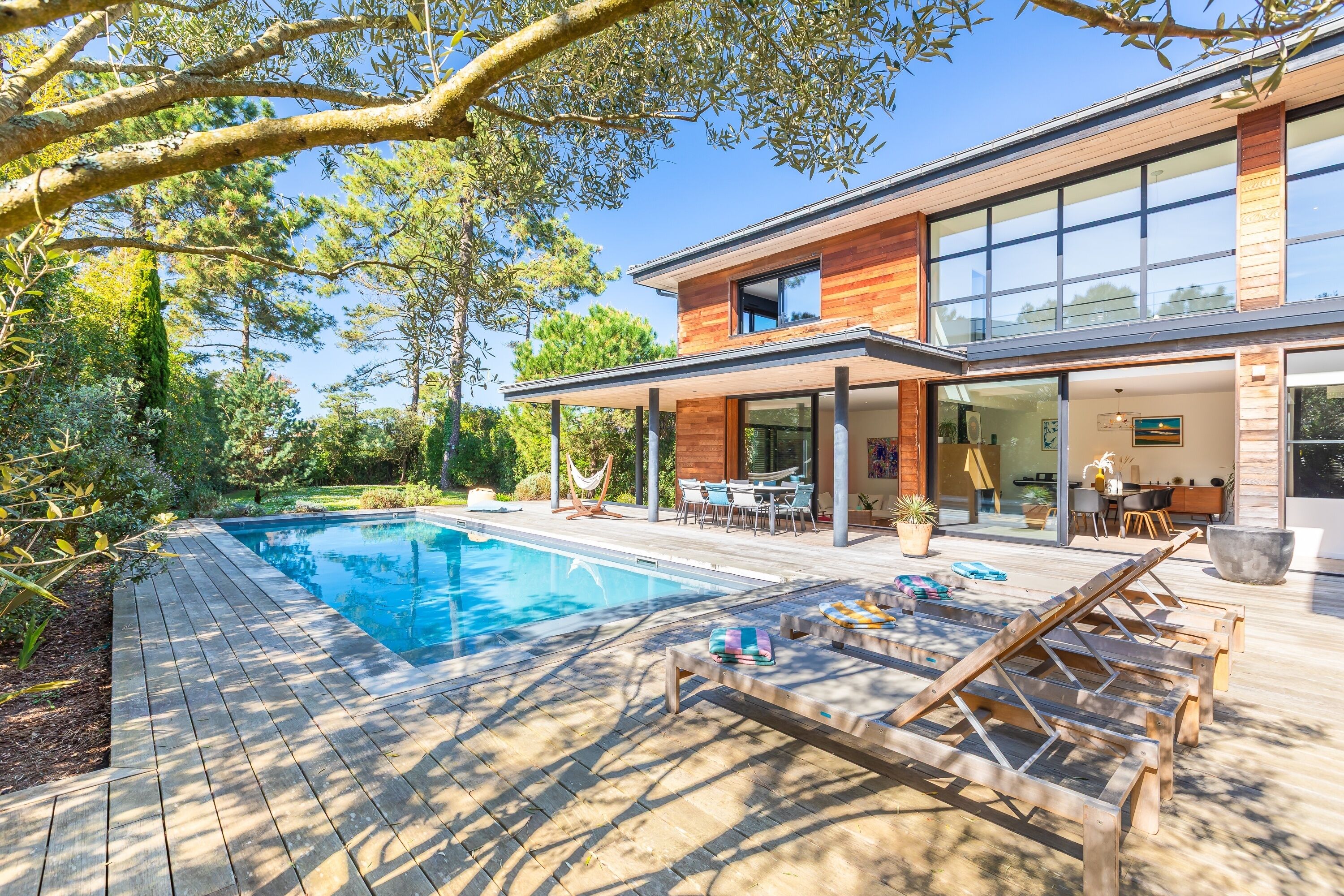 Ein modernes Haus mit Swimmingpool, Holzterrasse und Gartenmöbeln.