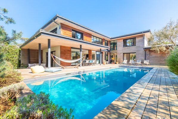 A modern two-story house with a swimming pool, outdoor seating, and a hammock.