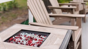 En patio med Adirondack-stole og et firkantet bord med glasplade.