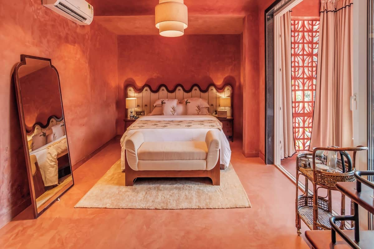 A bedroom with a bed, a nightstand, a mirror, a hanging light fixture, and a window with a decorative screen.