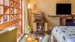 Une chambre d’hôtel avec un lit, une télévision, une petite table avec une lampe et une tasse, et une fenêtre agrémentée d’un paravent décoratif.