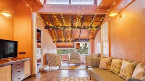 Un salon chaleureux avec un plafond en bois, des guirlandes lumineuses, un canapé, des fauteuils et un téléviseur.