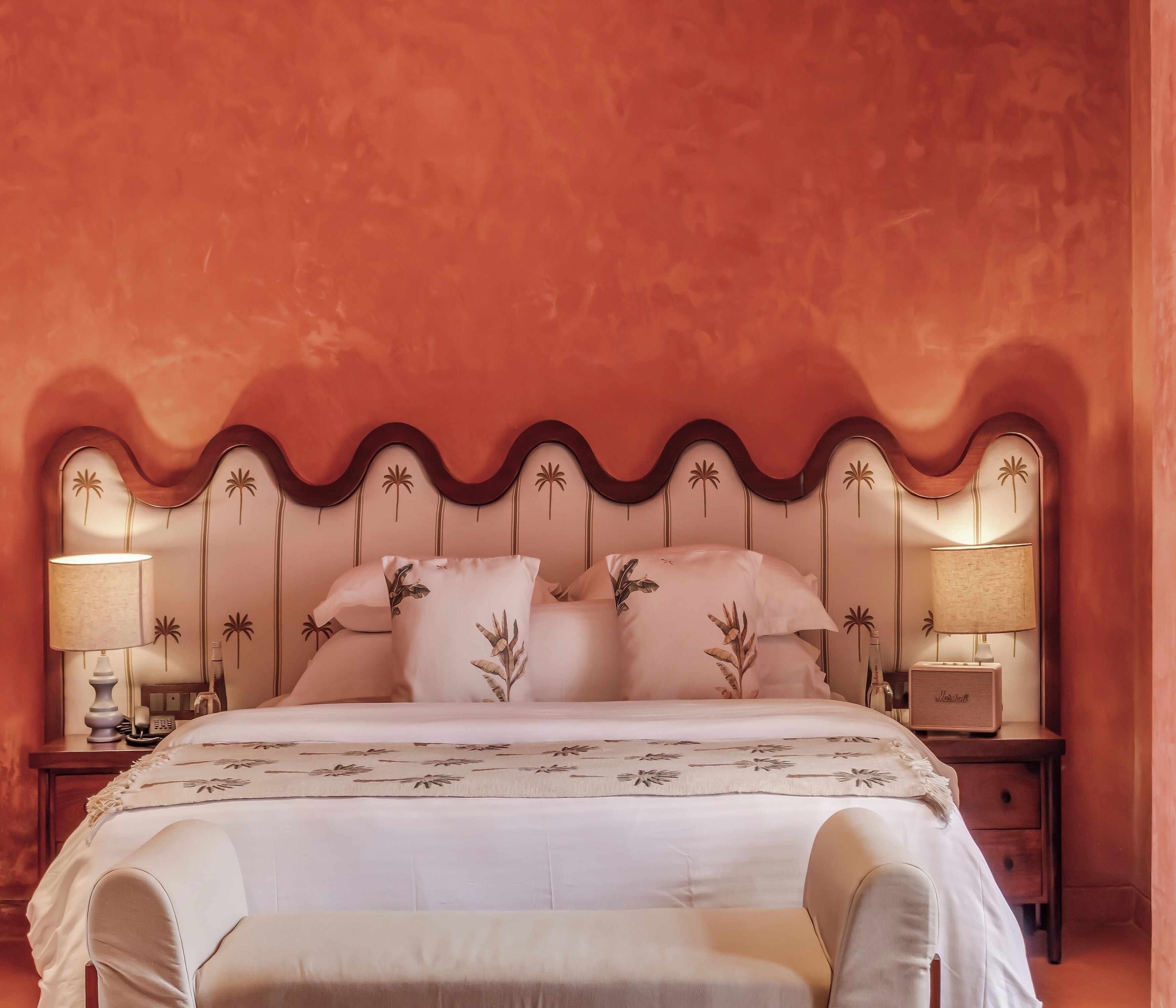 A bed with a wavy headboard, two bedside lamps, and a bedside table with a lamp and a bottle.