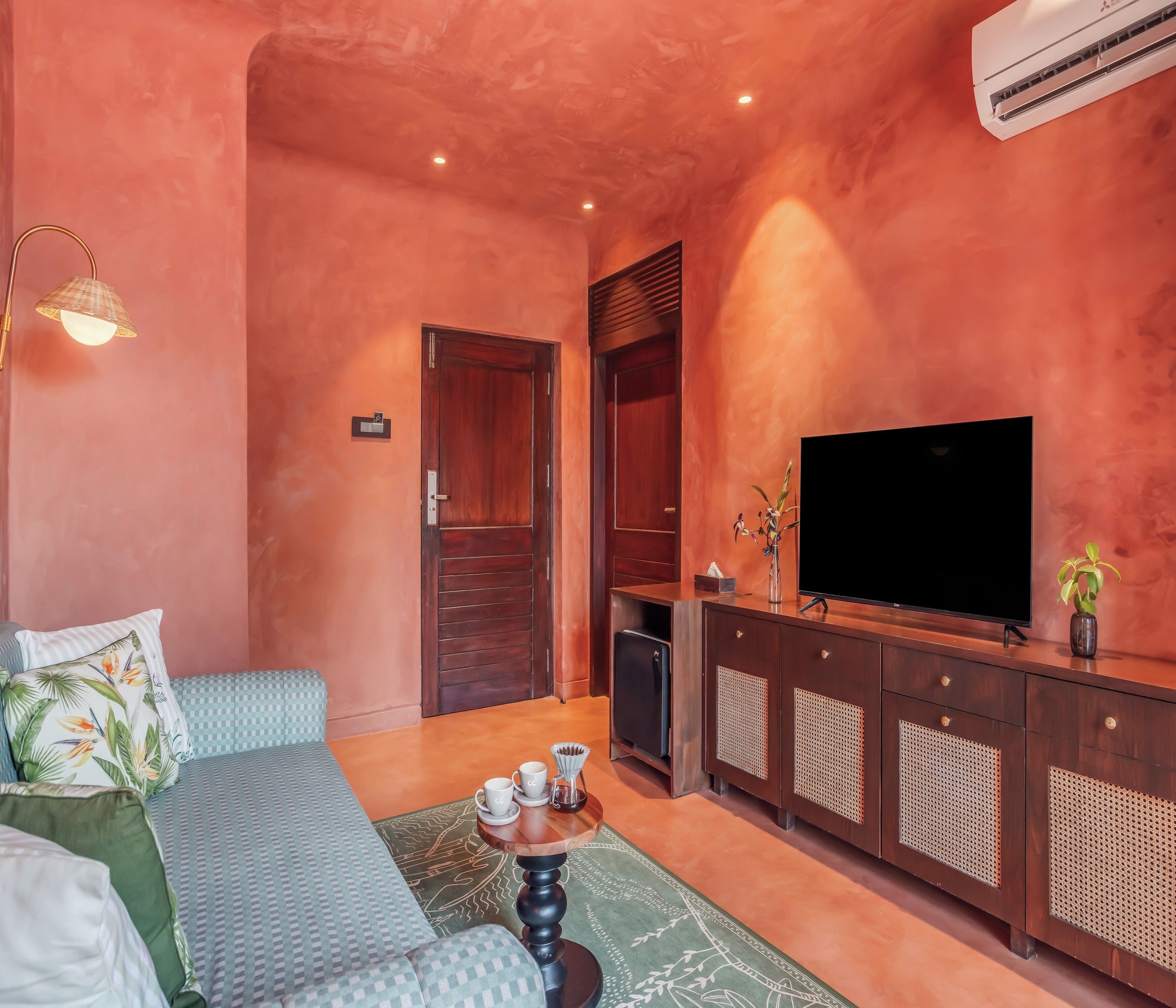 A cozy living room with a large flat-screen TV, wooden furniture, and a green patterned rug.