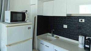 Une cuisine compacte avec un four à micro-ondes posé sur un réfrigérateur blanc, un plan de travail noir carrelé, un évier avec un robinet et une machine à café sur le comptoir.