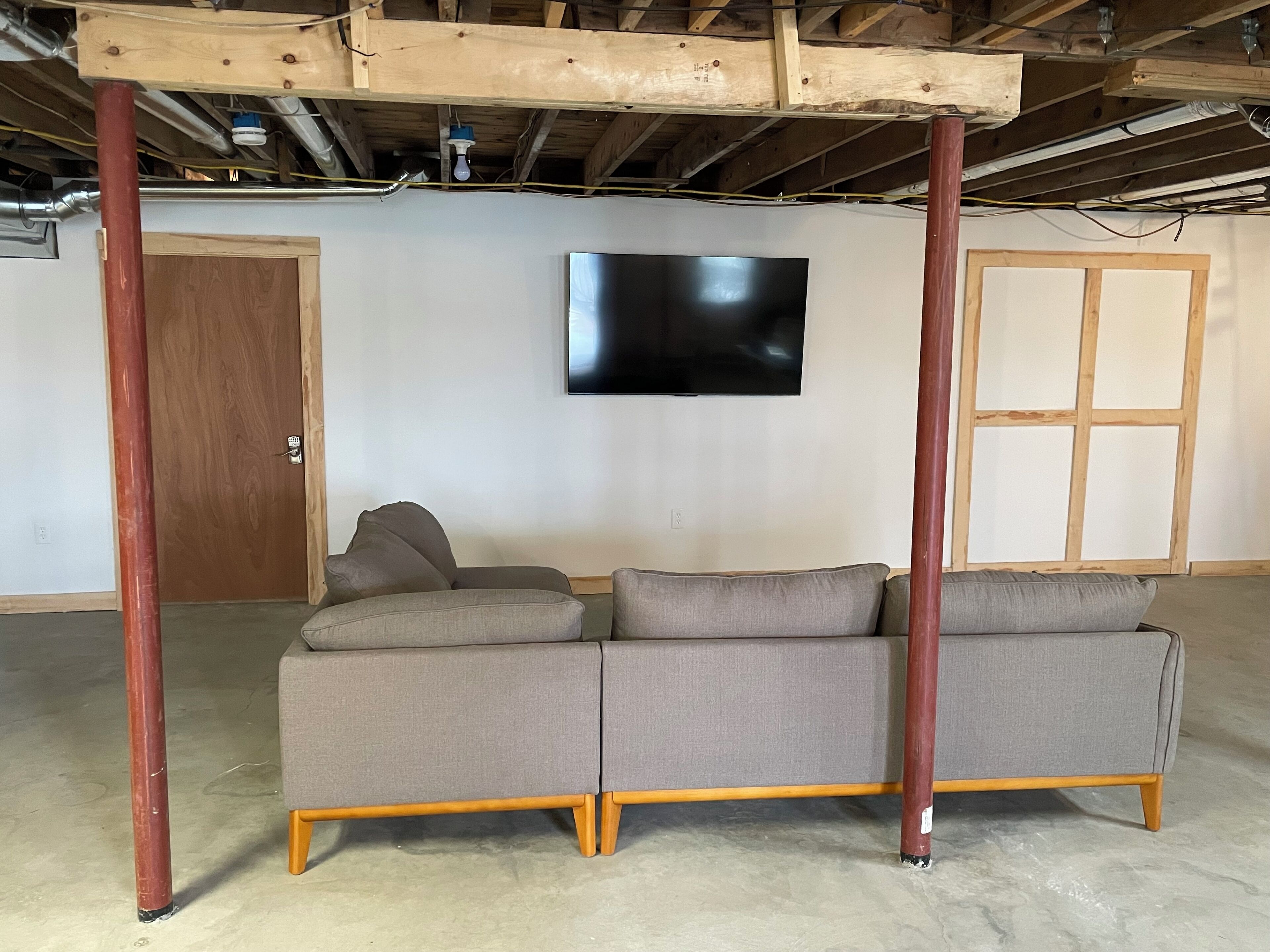 A room with a sectional sofa, wooden beams, a television, and a door.