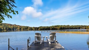 A wooden dock with two chairs facing a calm lake, surrounded by trees and a clear sky. - Sawyer Lake NH, Lake & Ski – 4BR, all the amenities for Year-Round Adventure! (Gilmanton)