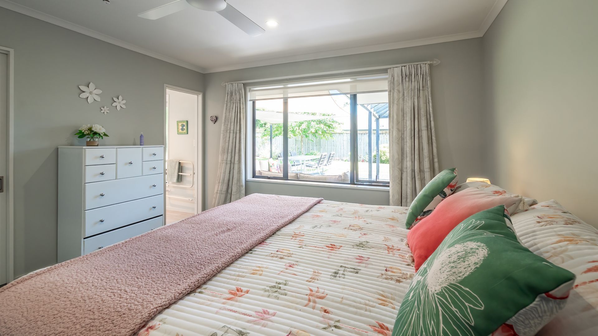 A bedroom with a bed, a dresser, a window with curtains, and a view of the outside.
