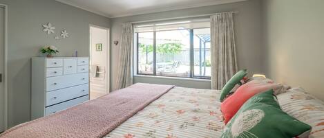 A bedroom with a bed, a dresser, a window with curtains, and a view of the outside.