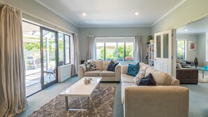 Un salon spacieux avec un canapé beige, une table basse et une vue sur le jardin grâce à de grandes portes-fenêtres coulissantes.