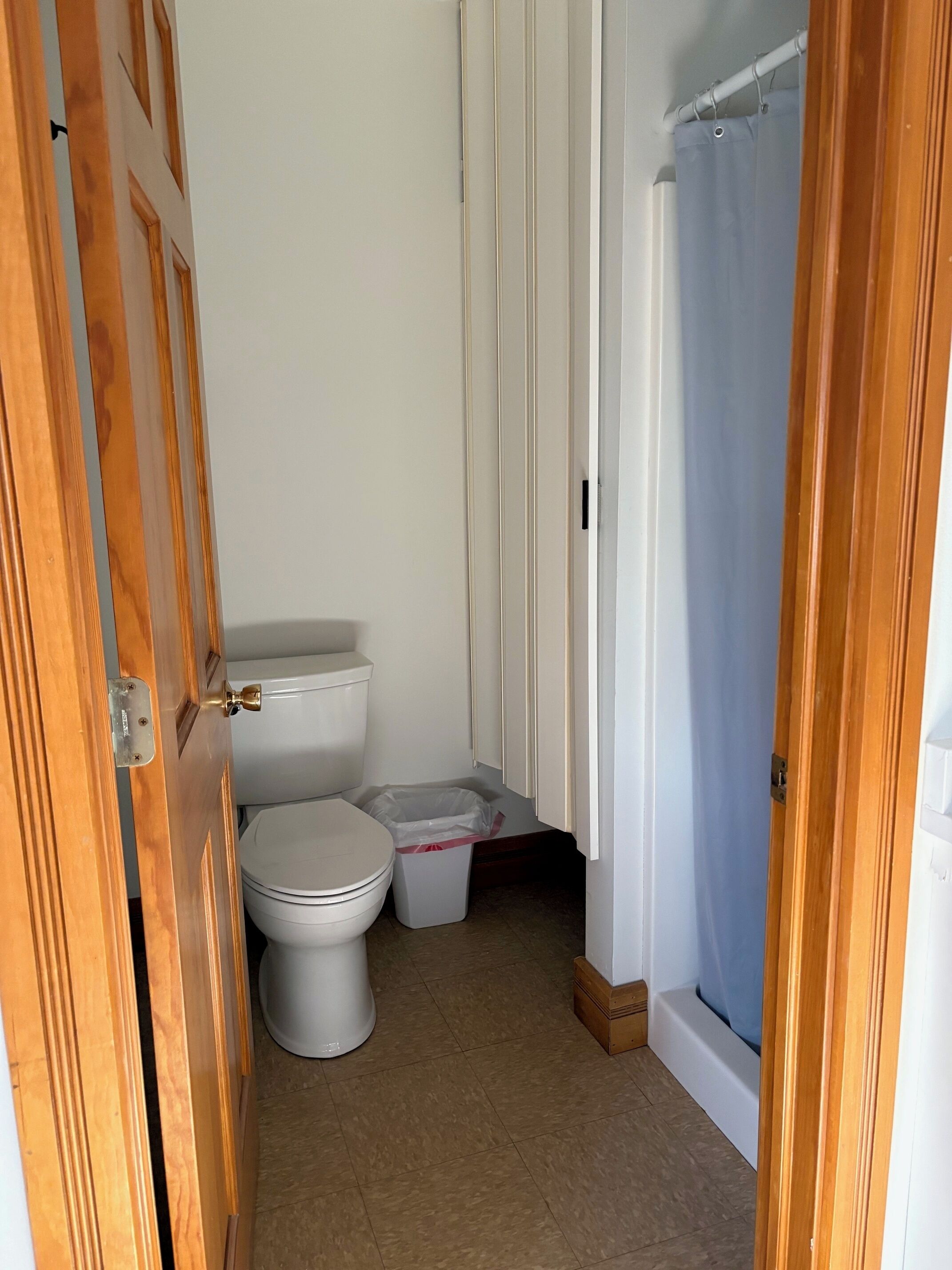 Une salle de bain comprenant des toilettes, une poubelle et un espace douche.