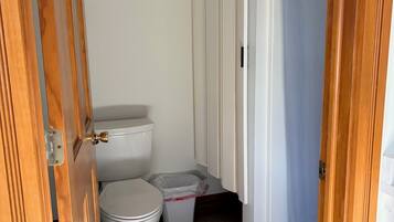 Une salle de bain comprenant des toilettes, une poubelle et un espace douche.