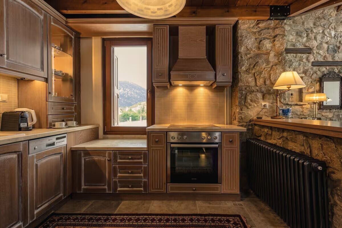 Una cocina con armarios de madera, horno empotrado, pared de piedra y ventana con vistas.