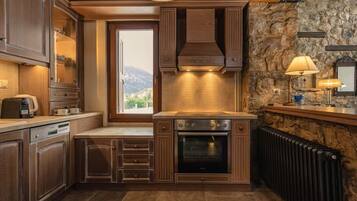 Una cocina con armarios de madera, horno empotrado, pared de piedra y ventana con vistas.