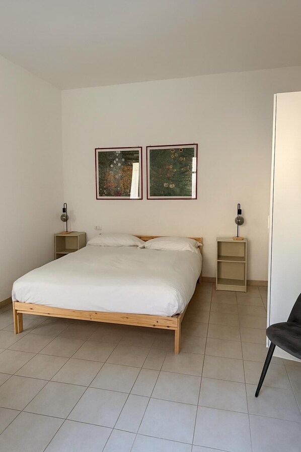 Ein Schlafzimmer mit einem hölzernen Bett, zwei Nachttischen und zwei gerahmten Kunstwerken an der Wand.