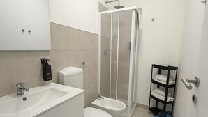 A modern bathroom with a white sink, toilet, and bidet, a glass shower enclosure, and a black towel rack. - Judith Room (Ciriè)