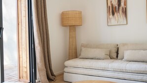 A modern living room with a sofa, a round table, a lamp, and a large window with curtains. - Villa Cala Rossa (Lecci)