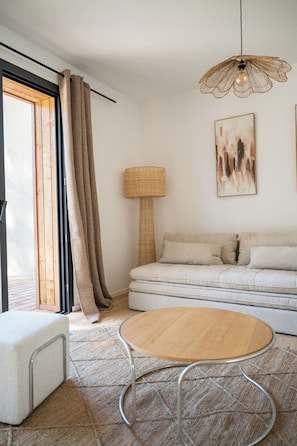 Ein stilvolles Wohnzimmer mit einer Couch, einem runden Tisch, einer Lampe und einem großen Fenster mit Vorhängen.
