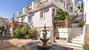 Un patio con una fuente, muros de piedra y una escalera que lleva a un nivel superior.