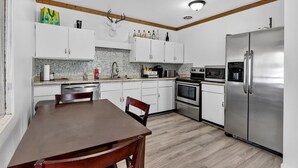 A modern kitchen with white cabinets, a stainless steel refrigerator, and a wooden dining table. - Alpine Getaway Steps from the Slopes (Brian Head)