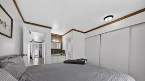 A bedroom with a bed, a suitcase, and a view into the kitchen area. - Alpine Getaway Steps from the Slopes (Brian Head)