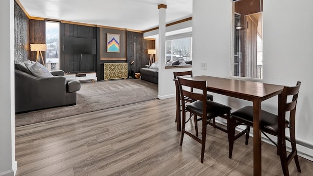 A modern living room with a dark sofa, a wooden dining table with chairs, and a large flat-screen TV. - Alpine Getaway Steps from the Slopes (Brian Head)