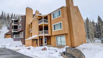 A multi-story building with balconies, large windows, and a snow-covered ground.
