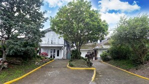 A building with a paved entrance area, surrounded by trees and greenery. - Villa Agape Near Puncak By ARBA (Cipanas)