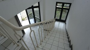 A staircase with white railings and black steps leading to a landing with large windows. - Villa Agape Near Puncak By ARBA (Cipanas)