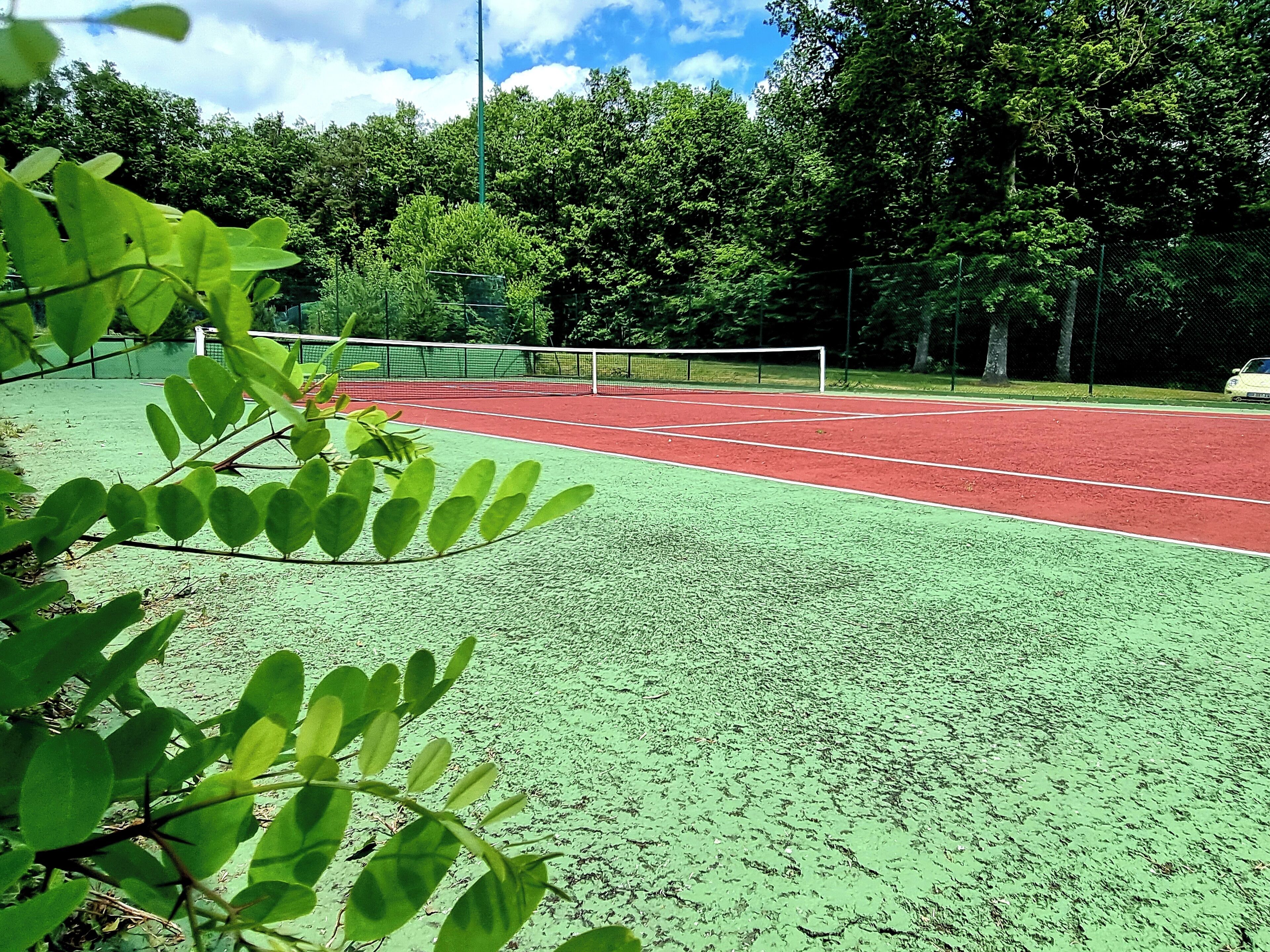 A tennis court with a green and red surface, surrounded by trees and a fence.