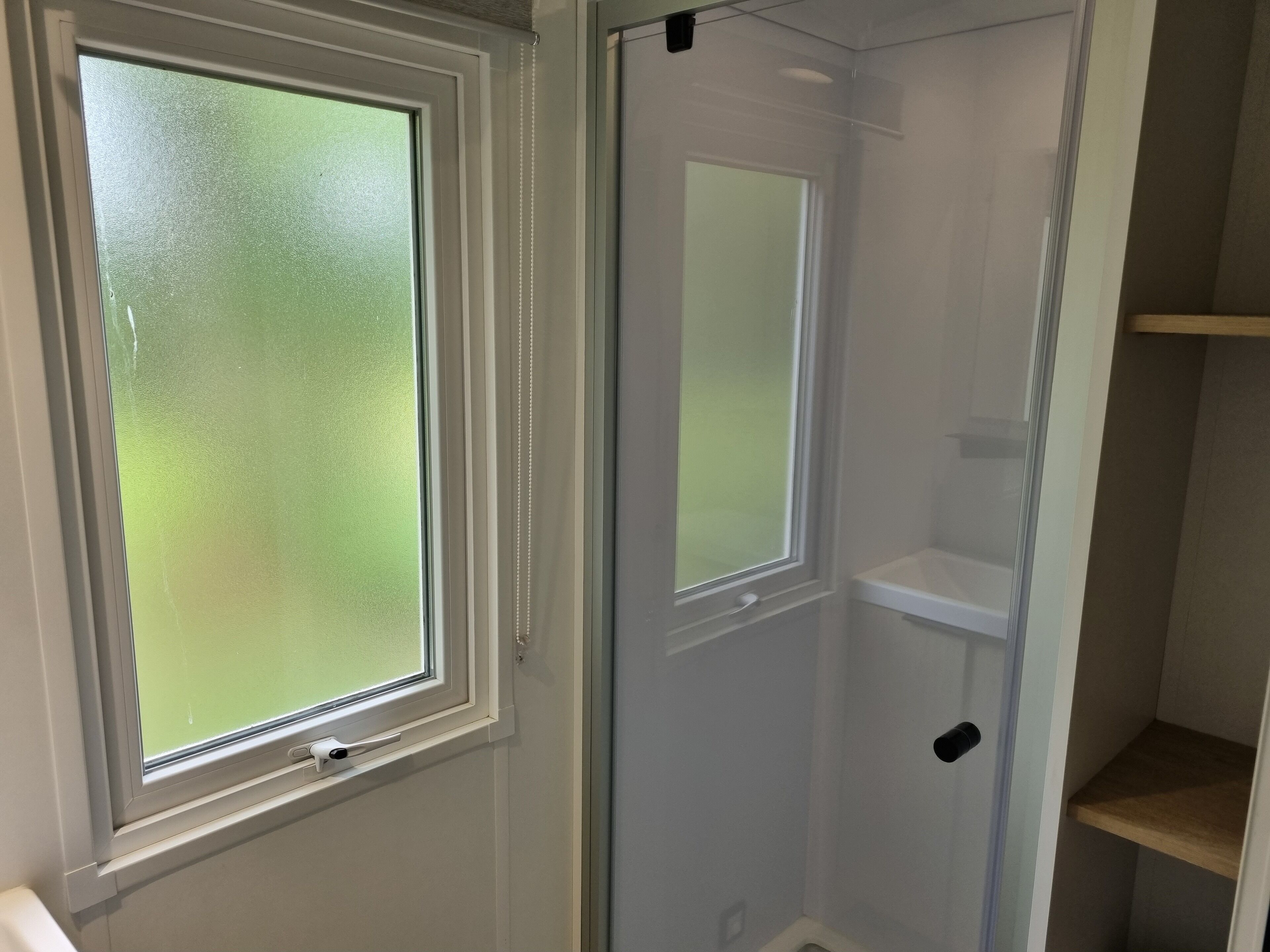 A bathroom with a frosted glass window, a white door, and a wooden shelf.