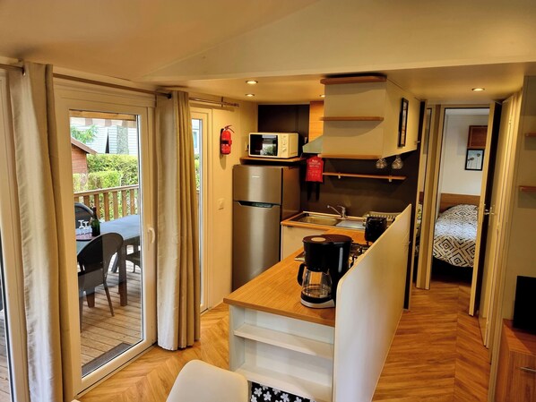 A compact kitchen with a refrigerator, microwave, and coffee maker. There is a dining area with a table and chairs, and a bedroom with a bed.