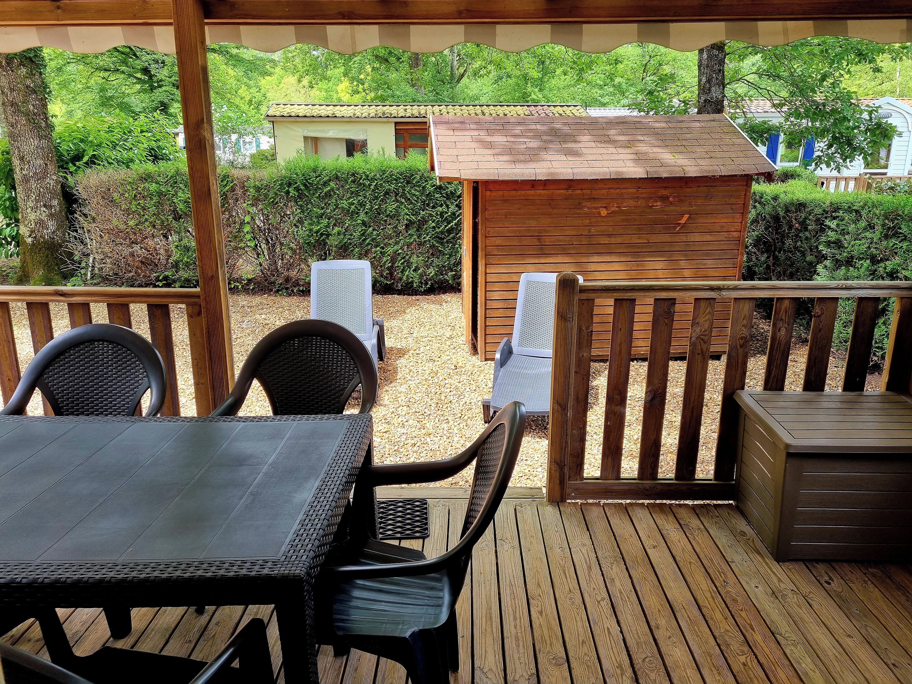 A covered patio with a table and chairs, a wooden deck, and a small shed.