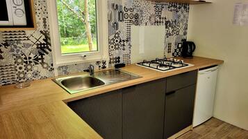 A compact kitchen with a sink, stove, and white dishwasher. A window provides a view of greenery outside.
