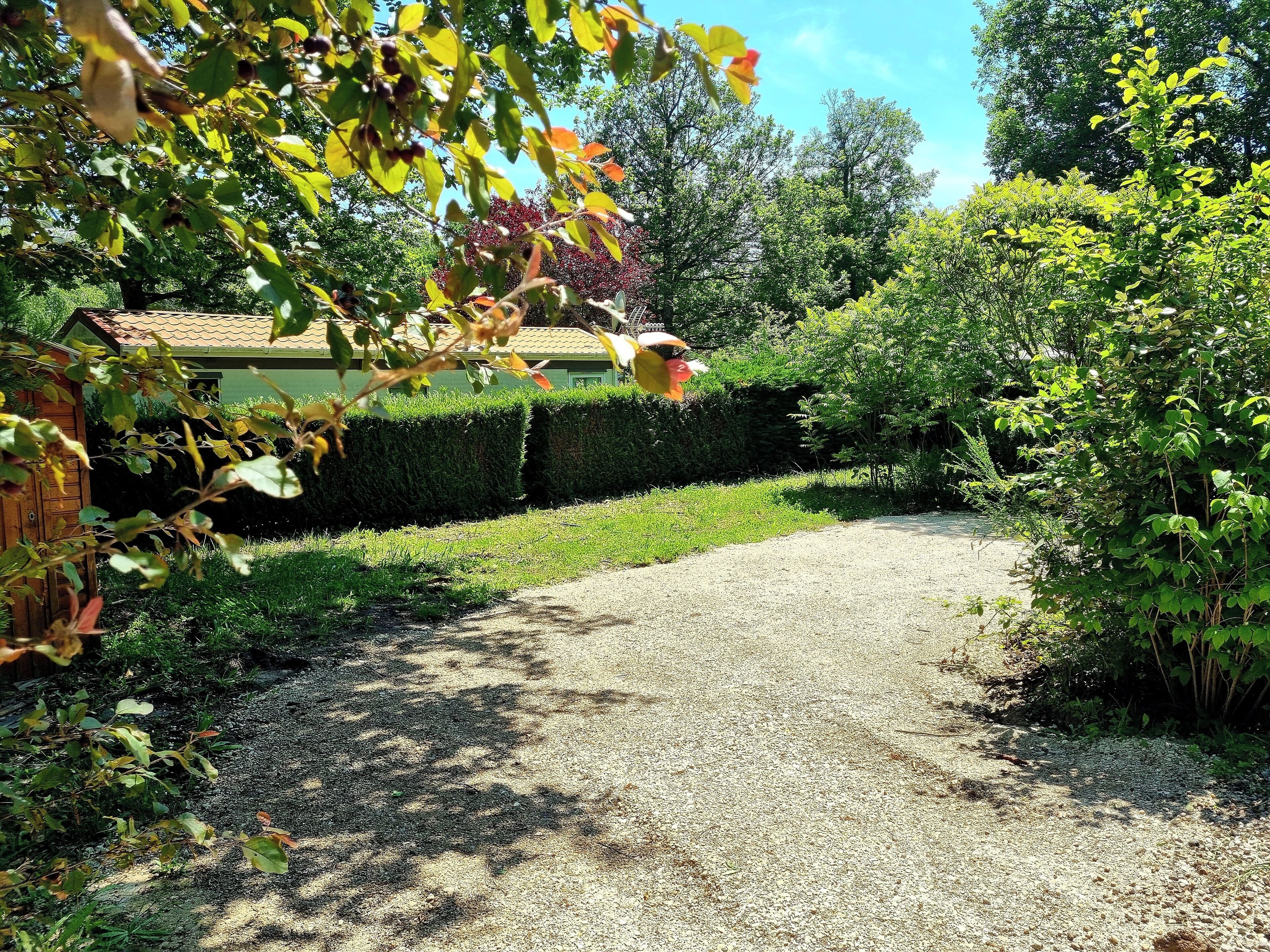 Un chemin de gravier mène à un bâtiment doté d’un toit végétalisé, entouré de haies et d’arbres bien entretenus.