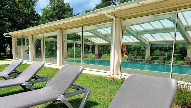 Et poolområde med liggestole og en bygning med glasfacade.