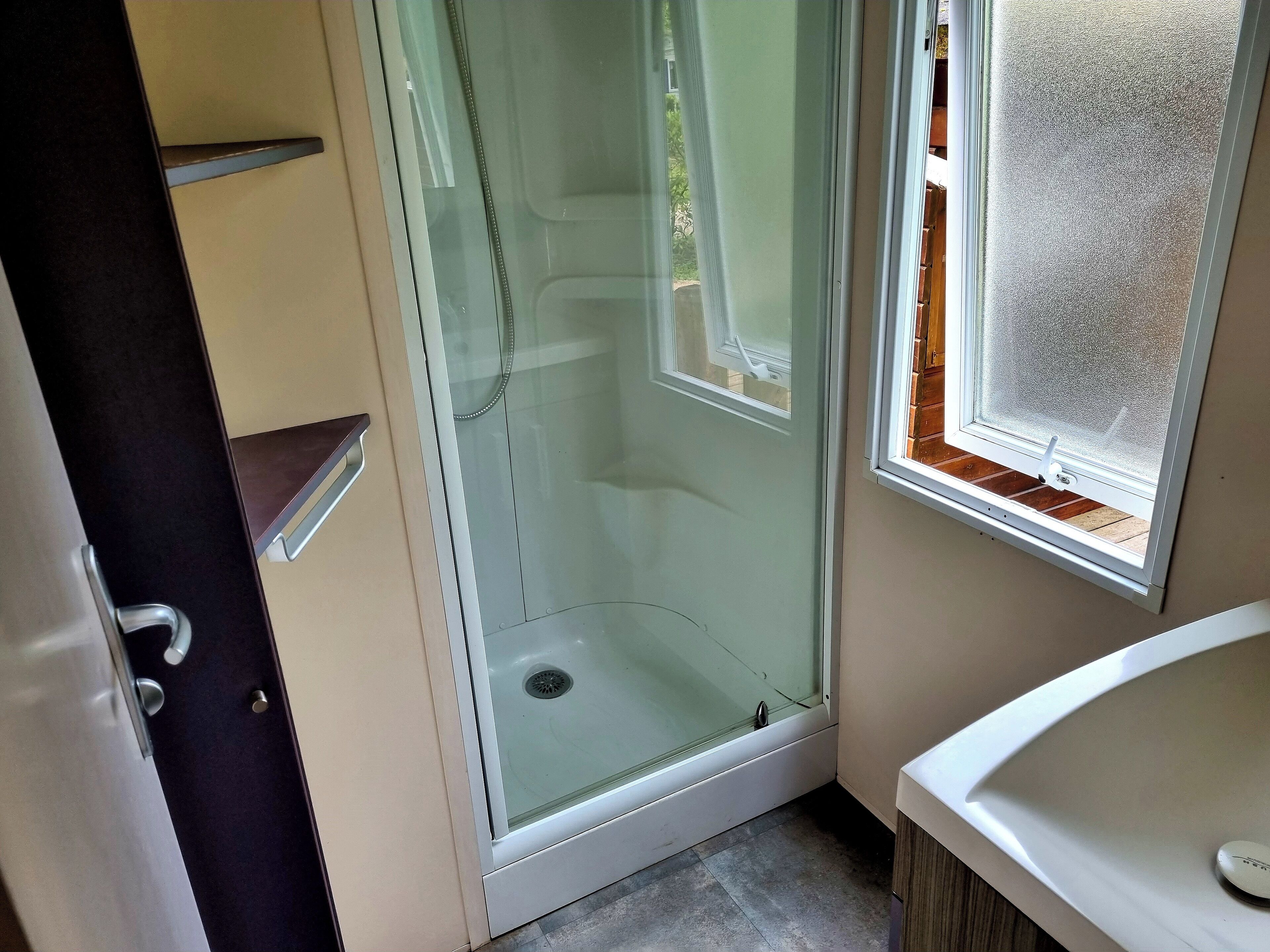 Un baño con cabina de ducha de vidrio, lavamanos y ventana con vidrio esmerilado.