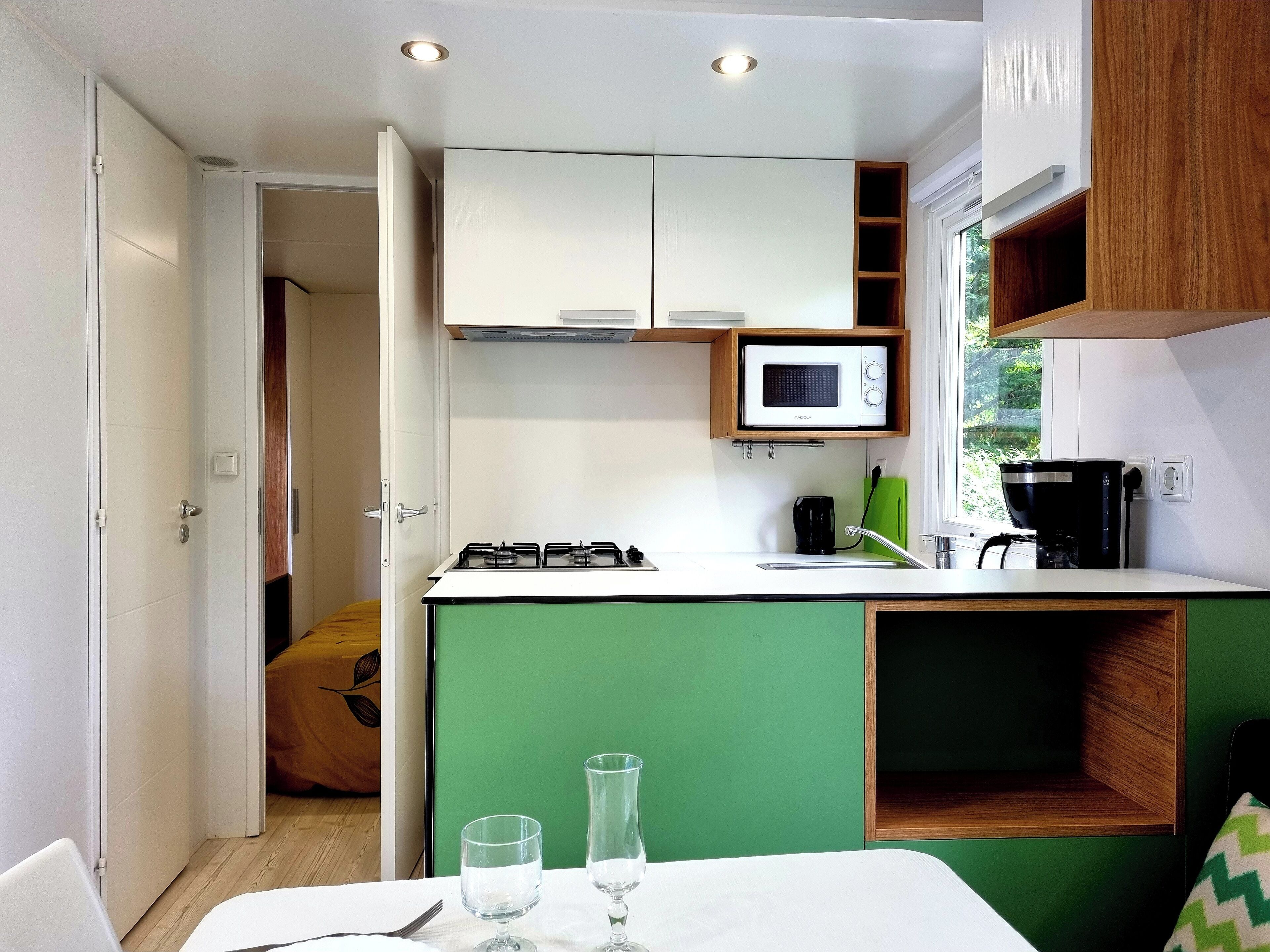 Cozinha compacta com micro-ondas, fogão e cafeteira, e área de jantar com mesa posta para dois.