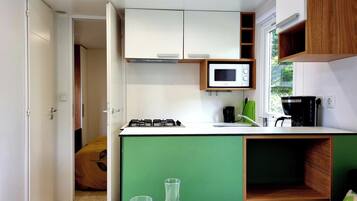 Cozinha compacta com micro-ondas, fogão e cafeteira, e área de jantar com mesa posta para dois.