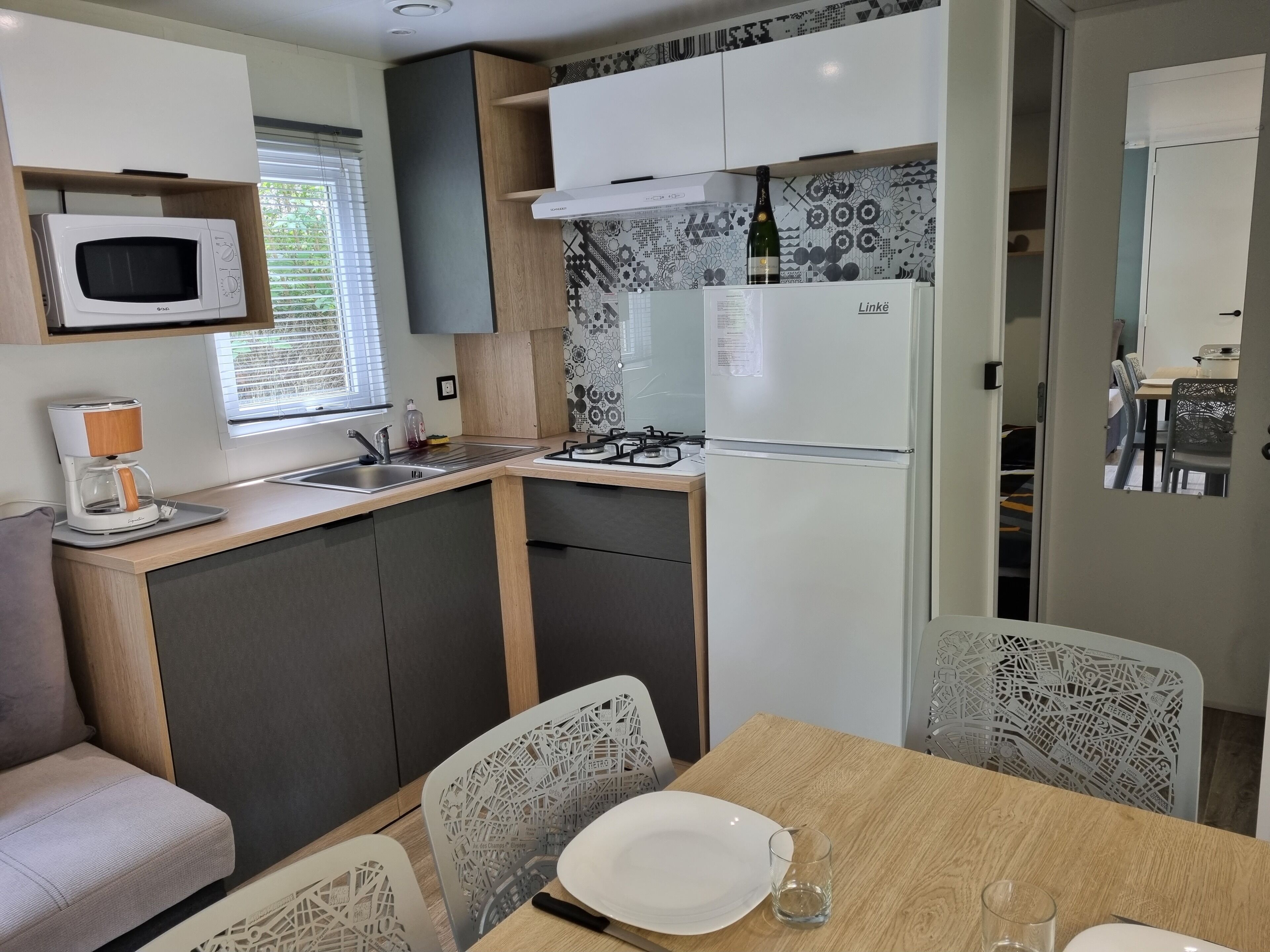 Een compacte keuken met een magnetron, koffiezetapparaat en een Linke koelkast. Een eethoek met een tafel en stoelen is zichtbaar.