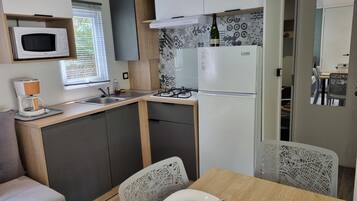 Een compacte keuken met een magnetron, koffiezetapparaat en een Linke koelkast. Een eethoek met een tafel en stoelen is zichtbaar.
